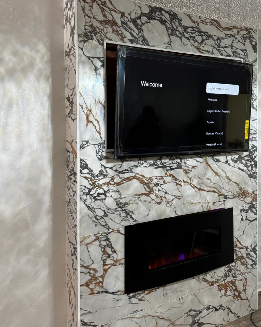 Floor-to-ceiling feature wall clad in book-matched marble-look porcelain slabs around a linear fireplace, veining aligned across every panel